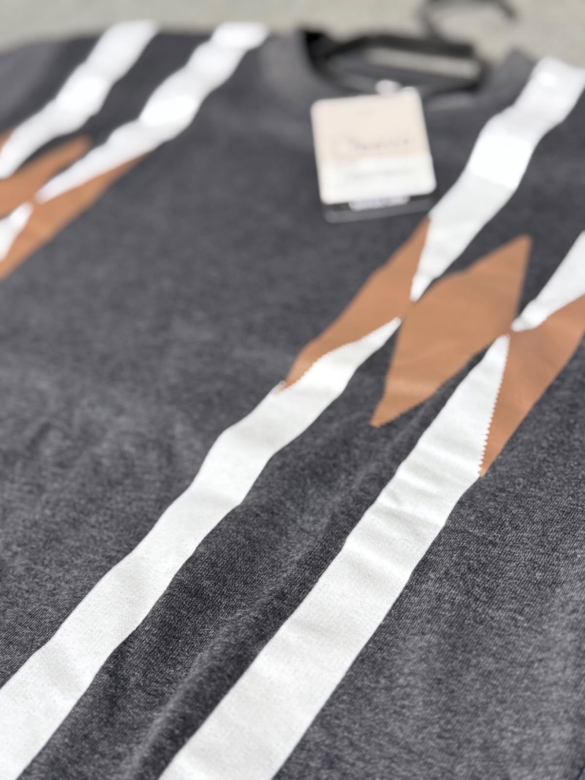 Close-up of a dark gray knit sweater with bold white vertical stripes and tan geometric accents, featuring a hangtag near the neckline.