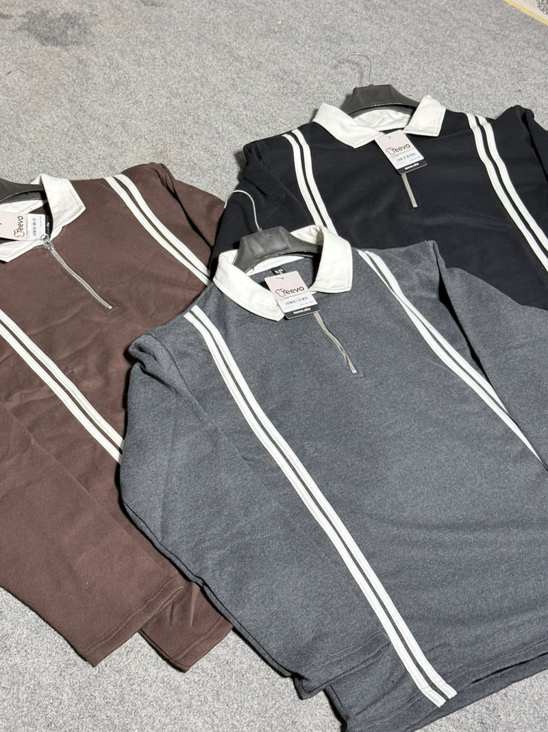 Three quarter-zip pullover sweaters laid flat on a gray textured surface, featuring white double stripes down the front and a contrasting white collar. The sweaters are shown in brown, dark gray, and black.