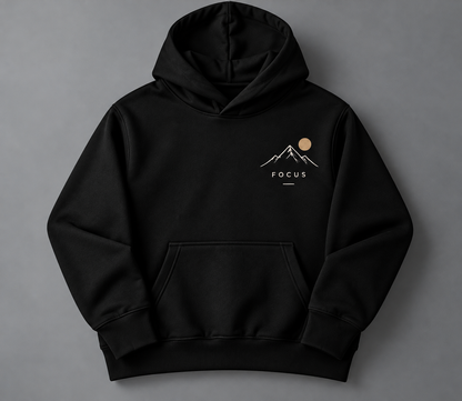 A black pullover hoodie with a small chest graphic showing a white mountain and sun design above the word 'FOCUS', displayed on a neutral gray background.
