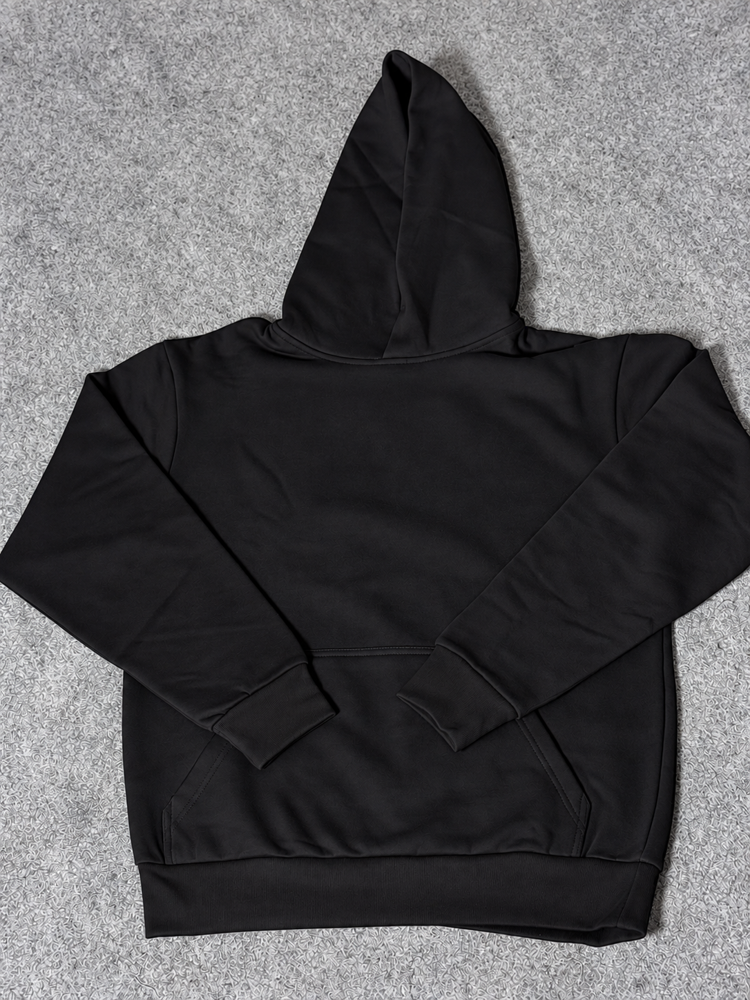 A black pullover hoodie laid flat on a textured gray background.