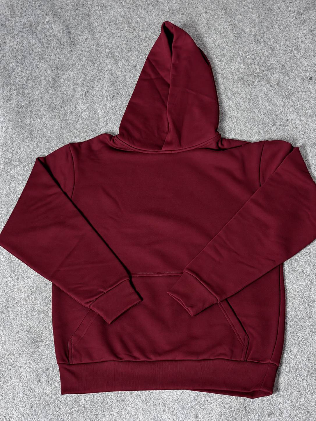 A dark burgundy pullover hoodie with a front kangaroo pocket, laid flat on a textured gray background.