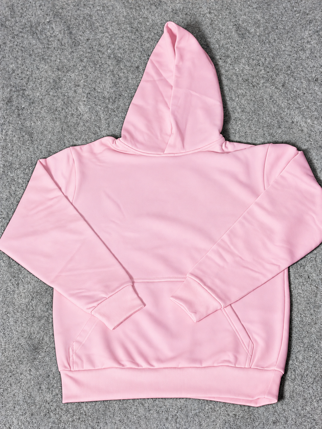 A light pink zip-up hoodie with a front kangaroo pocket, laid flat on a textured gray background.