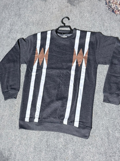 A dark gray crewneck sweatshirt with vertical white stripes and brown geometric diamond patterns on the chest, laid flat on a gray textured surface with a black hanger.