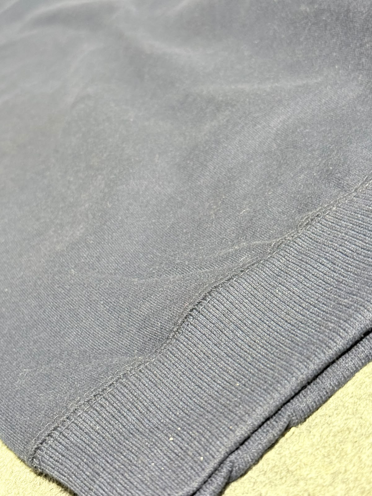 Close-up of a dark gray ribbed knit fabric, showing the texture and hem detail of a garment.