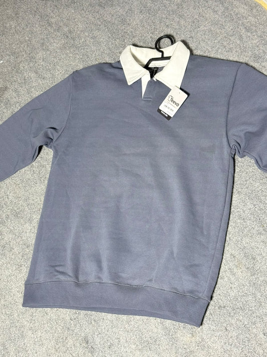 A gray long-sleeve polo shirt with a contrasting white collar, laid flat on a gray carpeted floor with a hangtag still attached.