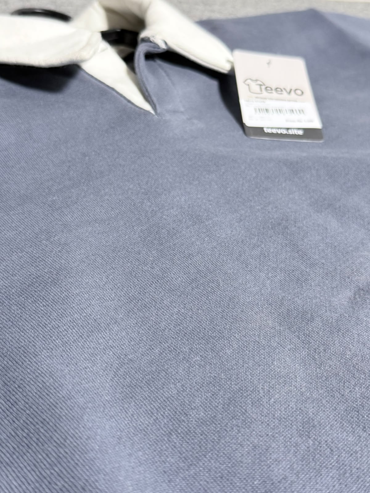 A close-up of a slate blue polo shirt with a white collar and a visible Teevo brand hangtag.