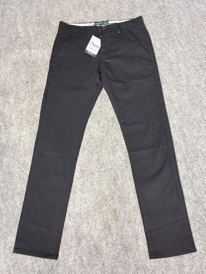 A pair of slim-fit black trousers laid flat on a gray carpet background, with a white retail tag attached near the waistband.