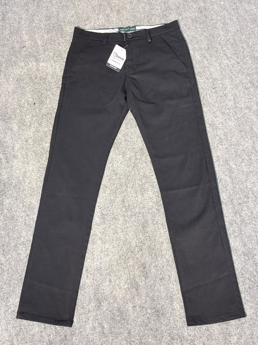 A pair of slim-fit black trousers laid flat on a gray carpet background, with a white retail tag attached near the waistband.