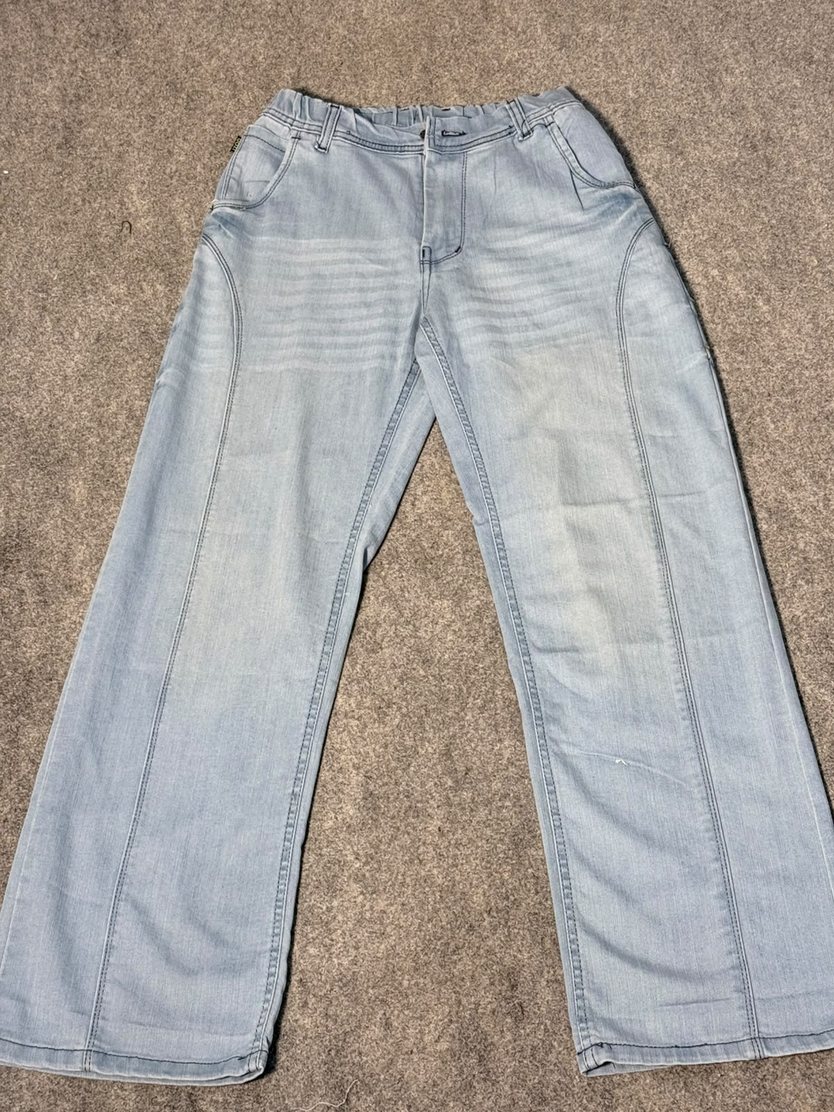 Light wash blue denim jeans laid flat on a textured gray carpet.