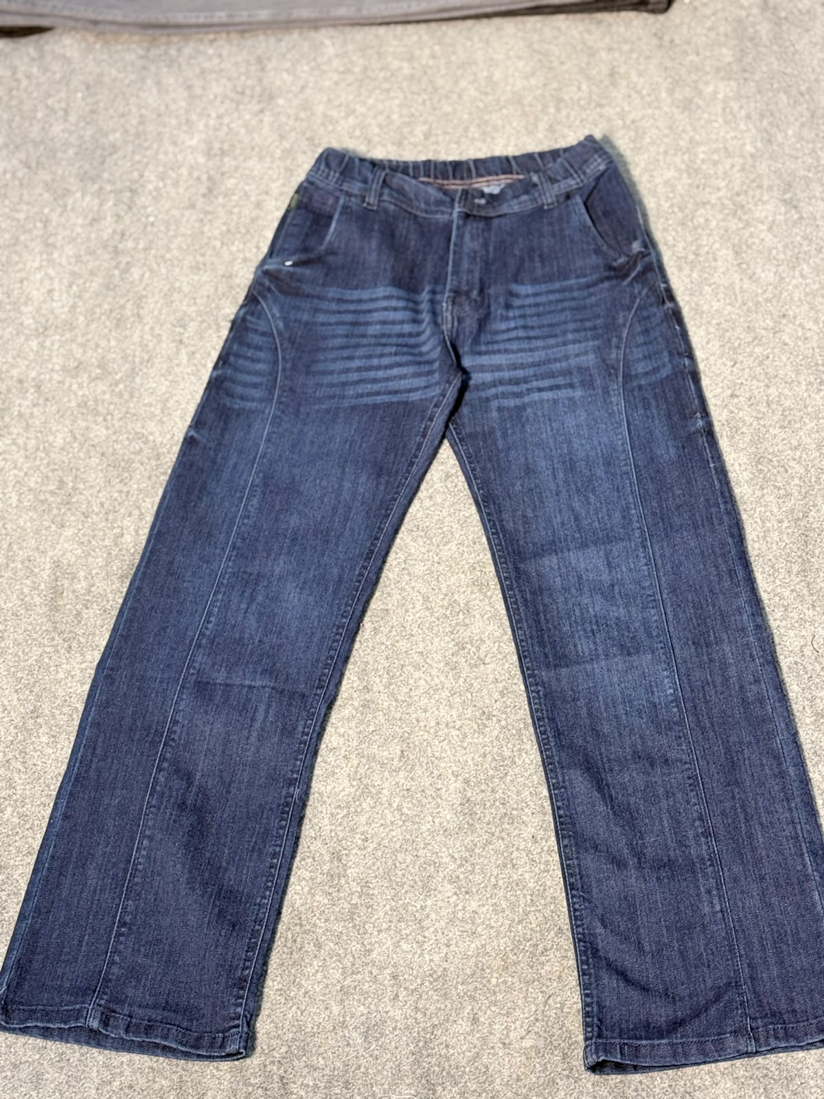 A pair of dark blue denim jeans laid flat on a textured gray carpet.