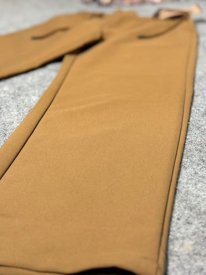 A close-up of a pair of solid mustard brown pants laid flat on a gray textured surface.