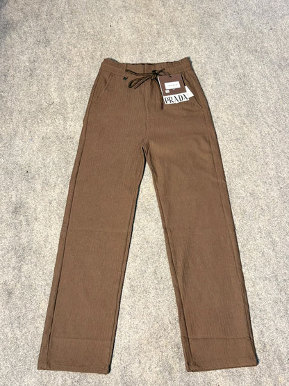 A pair of Prada brown corduroy trousers laid flat on a gray carpeted floor, featuring a drawstring waist and a white brand tag.