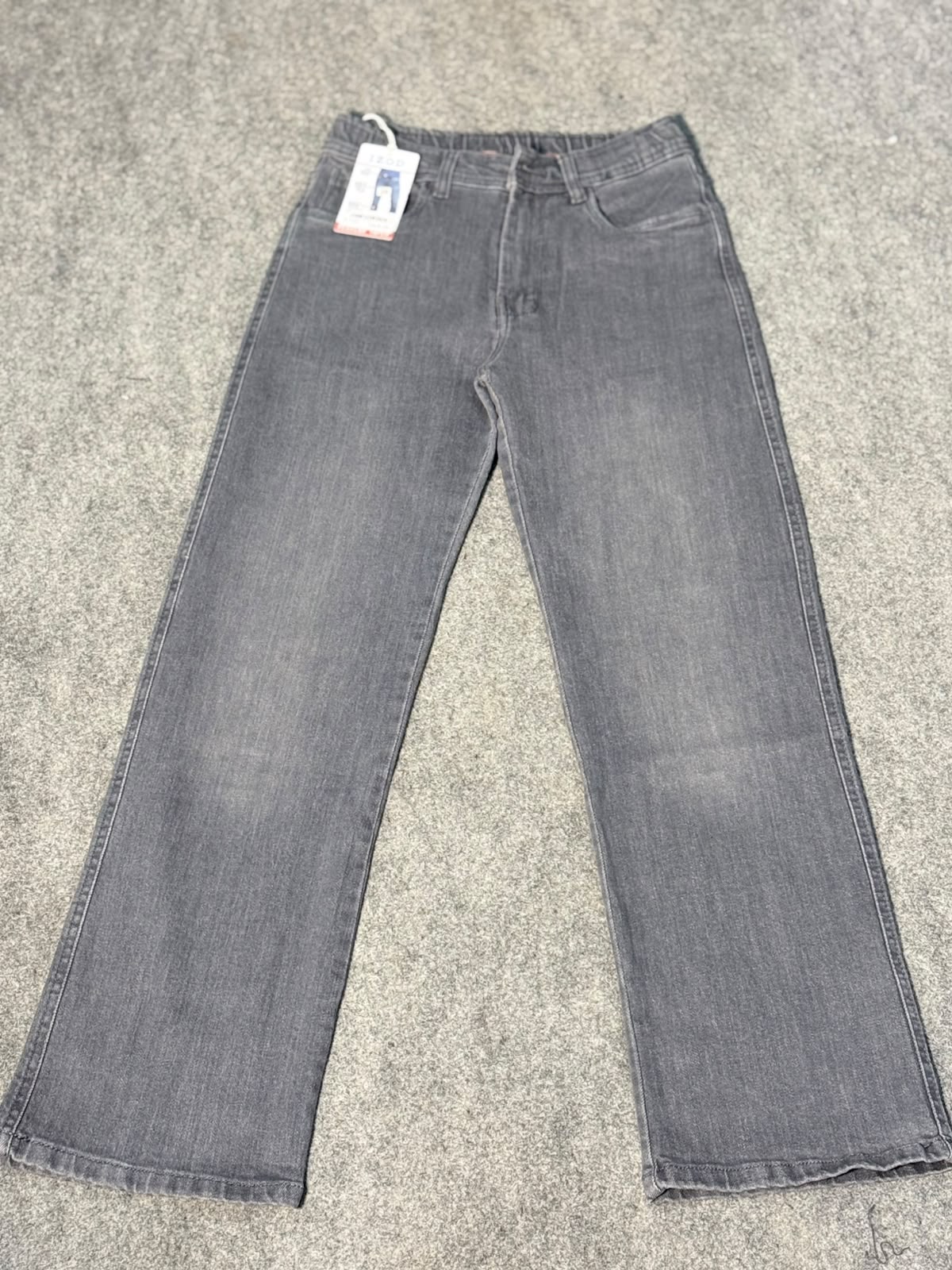 A pair of gray denim jeans with a slight flare, laid flat on a gray carpet. A white retail tag is attached near the waistband.