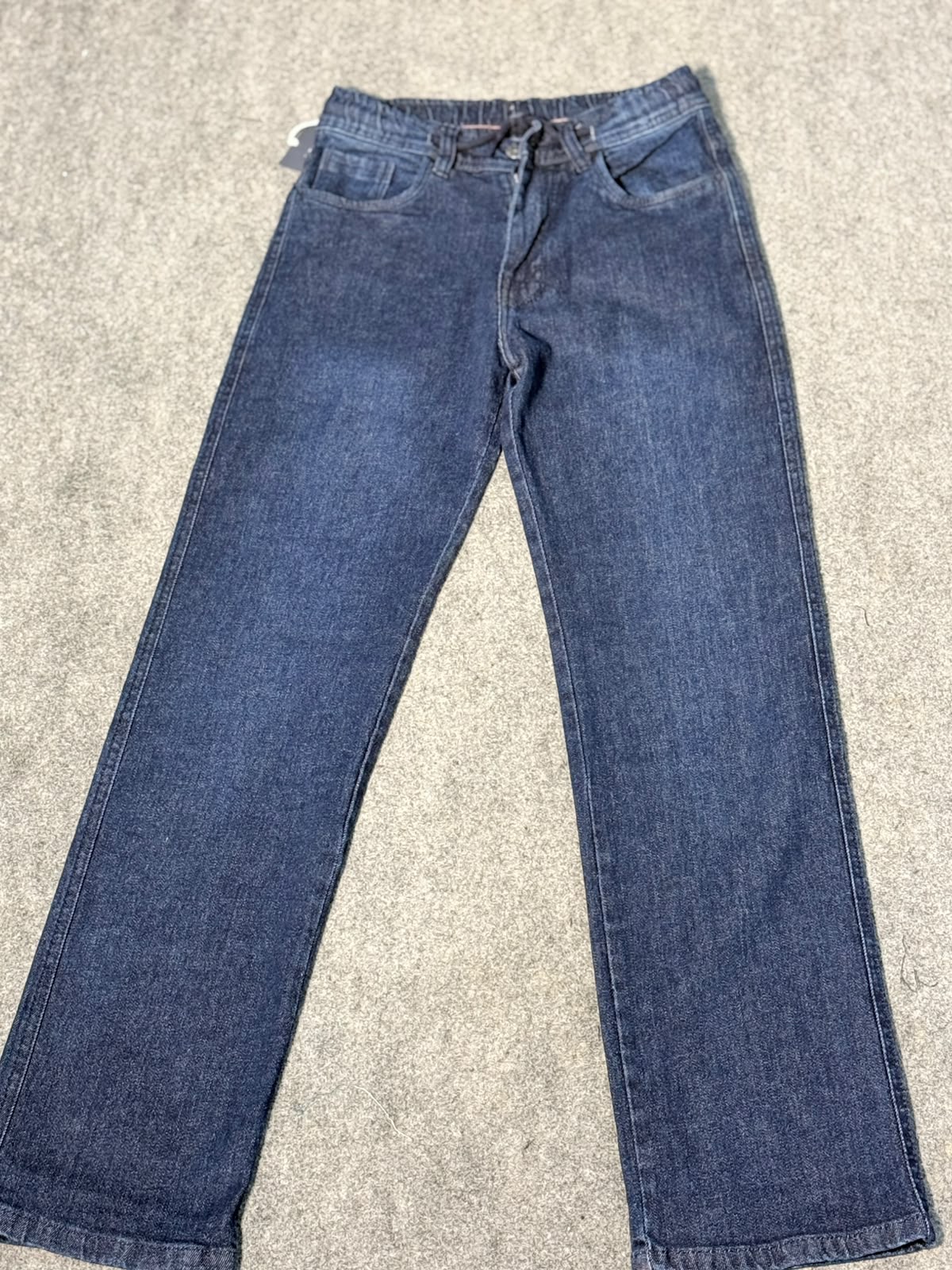 A pair of medium-wash blue denim jeans laid flat on a textured gray carpet.