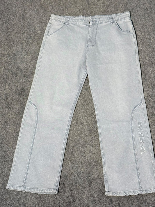 Light gray washed denim jeans laid flat on a gray textured surface, featuring a straight-to-slightly-flared leg with contrast stitching and vertical branding text on the lower right leg.