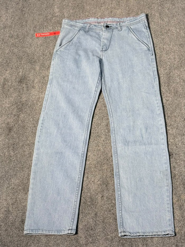 Light-wash blue denim jeans laid flat on a gray carpet, with a red brand tag visible at the waistband.