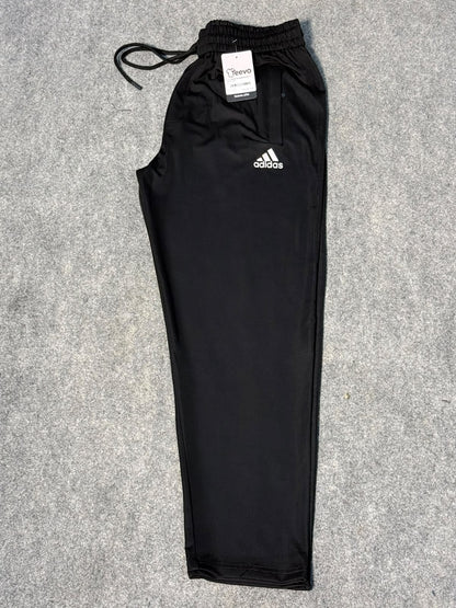 Black Adidas athletic pants with a white logo on the left chest, laid flat on a gray textured background.