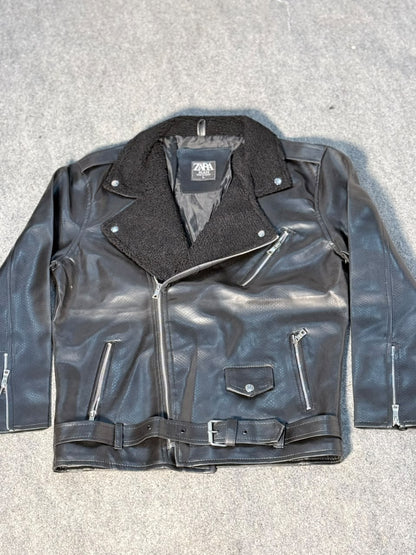 A black faux-leather biker jacket with a dark gray fleece collar, laid flat on a gray textured surface. The jacket features a zippered front, zippered pockets, and a matching belt.