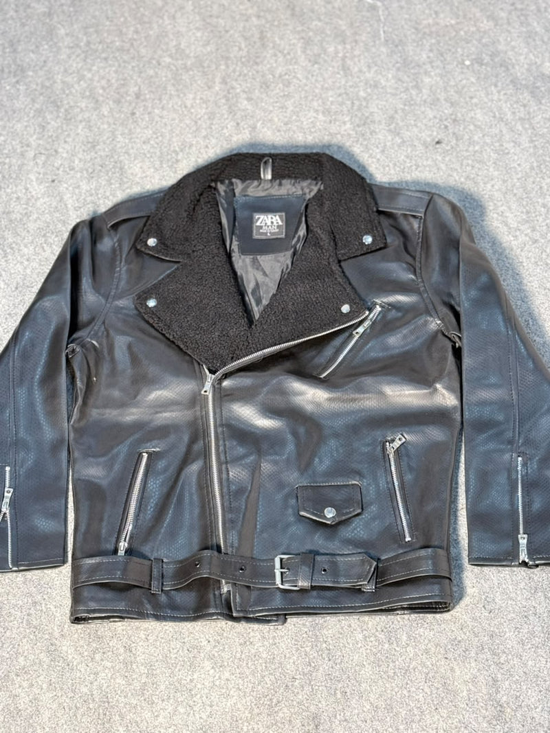 A black faux-leather biker jacket with a dark gray fleece collar, laid flat on a gray textured surface. The jacket features a zippered front, zippered pockets, and a matching belt.