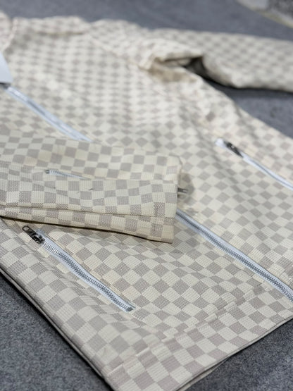 A beige and gray checkerboard patterned jacket with silver zippers, laid flat on a gray textured surface.