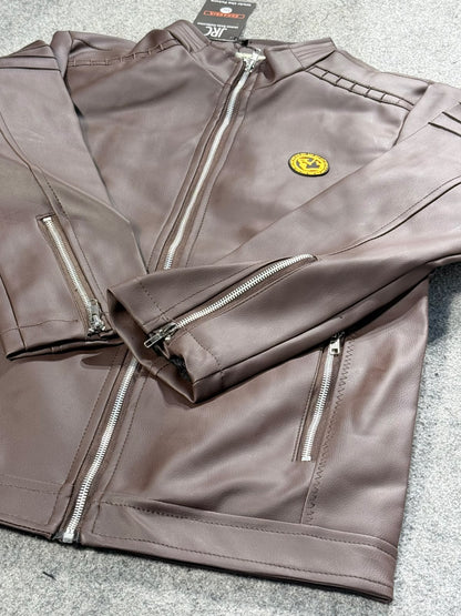 A brown faux-leather motorcycle jacket with silver zippers and a small yellow circular chest emblem, laid flat on a gray textured surface.