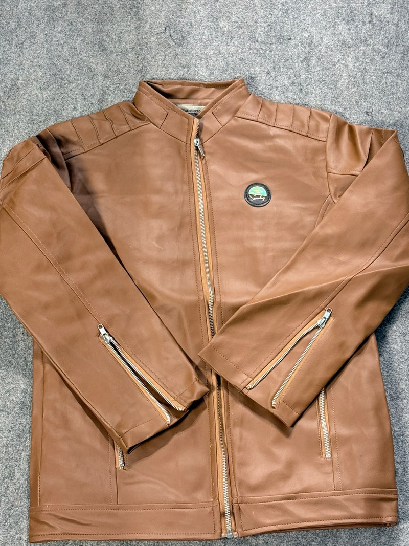 A brown faux-leather jacket with a stand collar, front zipper, and zippered sleeve cuffs, laid flat on a gray textured carpet. A circular green and black logo patch is visible on the left chest.