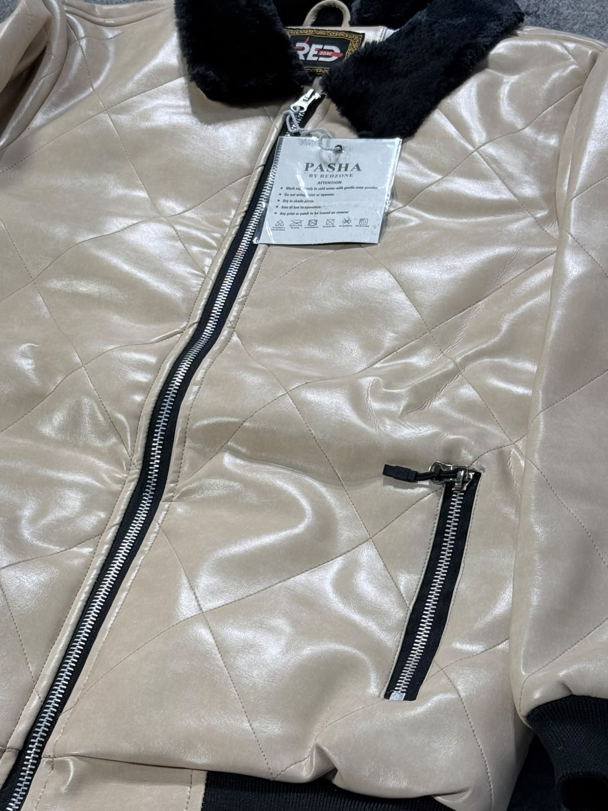A close-up of a beige quilted faux-leather jacket with a black fuzzy collar, black zipper details, and a visible 'FASHA' brand tag.