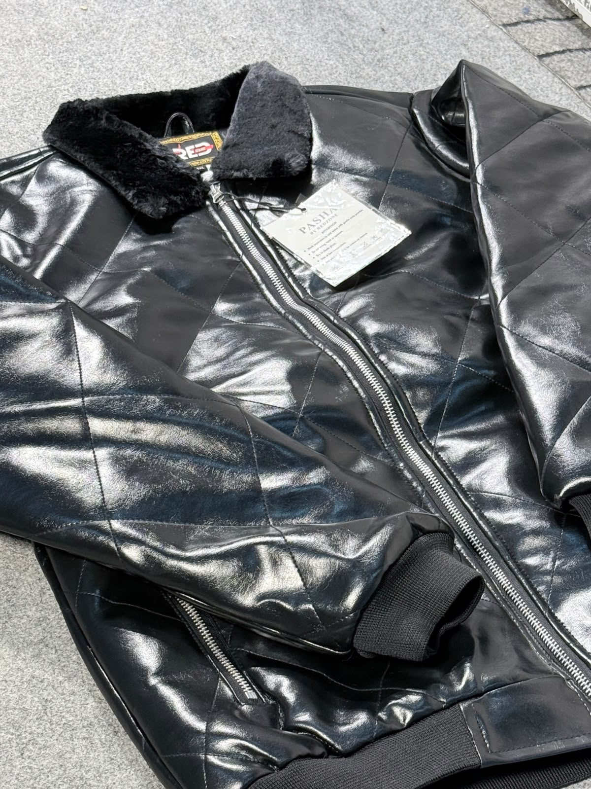 A black quilted faux-leather bomber jacket with a black faux-fur collar, laid flat on a gray paved surface. The jacket features a front zipper, ribbed cuffs, and a white product tag still attached.