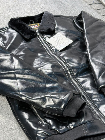 A black quilted faux-leather bomber jacket with a black faux-fur collar, laid flat on a gray paved surface. The jacket features a front zipper, ribbed cuffs, and a white product tag still attached.