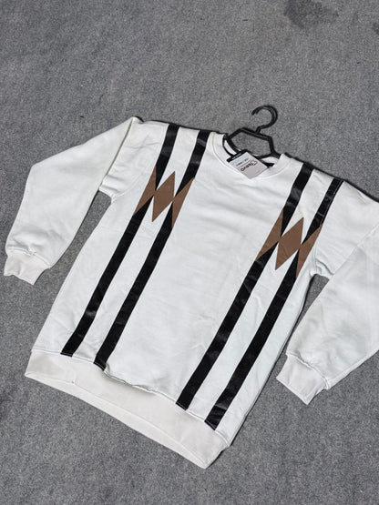 A white crewneck sweatshirt with bold black vertical stripes and brown lightning-bolt motifs on the chest, laid flat on a gray textured surface with a black hanger.